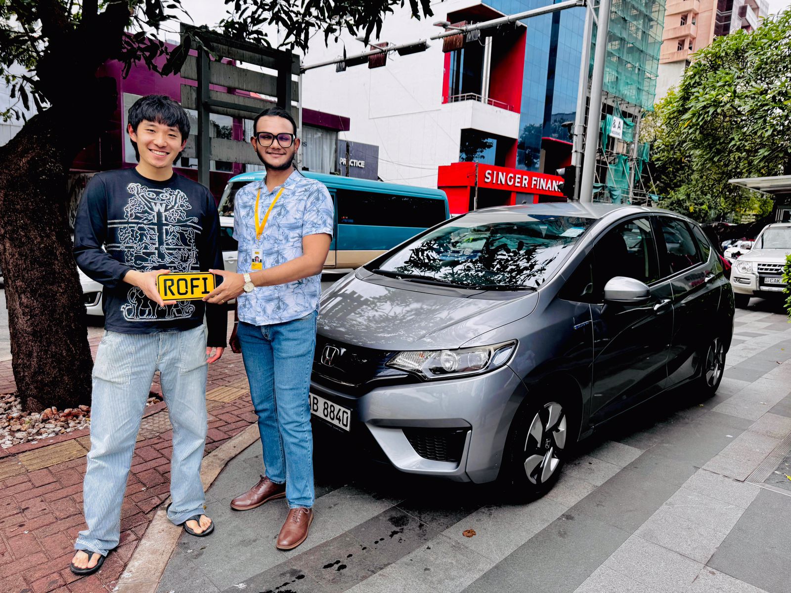 A happy Chinese customer is with the vehicle host in front of a Honda Fit vehicle.